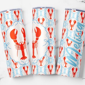 May include: Three white insulated tumblers with a red lobster pattern and blue accents. One tumbler has the name "Melissa" in light blue script. The design includes red lobsters, blue bows, and vertical blue stripes.