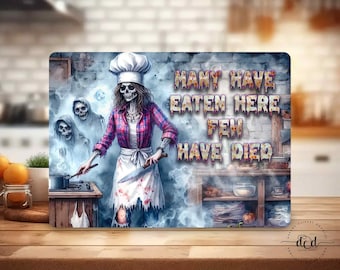 May include: A rectangular cutting board with a spooky chef skeleton illustration. The skeleton wears a chef's hat, a red plaid shirt, and a white apron, holding a knife and a cooking spoon. The text reads "MANY HAVE EATEN HERE FEW HAVE DIED."