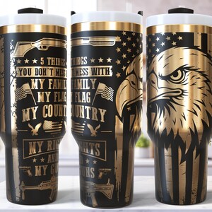 Op de afbeelding: Zwarte en gouden geïsoleerde reisbekers met handvatten. De bekers hebben patriottische ontwerpen, waaronder een Amerikaanse vlag, een adelaar en de tekst "5 dingen waar je niet mee moet sollen". De bekers hebben een witte rand en een zwart handvat.