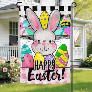 May include: A colourful Easter garden flag featuring a white bunny rabbit wearing a pink bow and surrounded by colourful eggs. The flag reads "Happy Easter!" in black text.