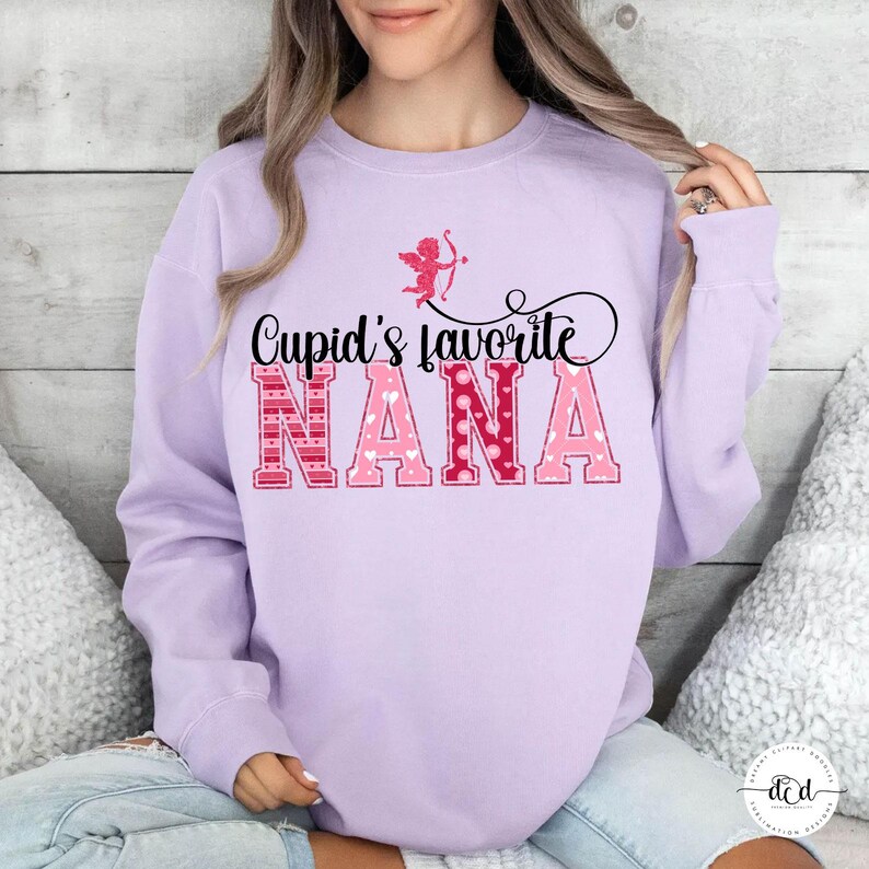 May include: A lilac sweatshirt featuring the phrase "Cupid's favourite NANA" in pink and red. A small Cupid graphic with a bow and arrow is above the text. The sweatshirt is a relaxed, casual style.