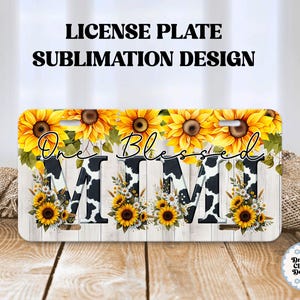 Puede incluir: Diseño de sublimación de placa de matrícula con girasoles y las palabras "One Blessed Mimi". Las letras "MIMI" tienen un diseño de estampado de vaca. El fondo es un patrón de vetas de madera clara.