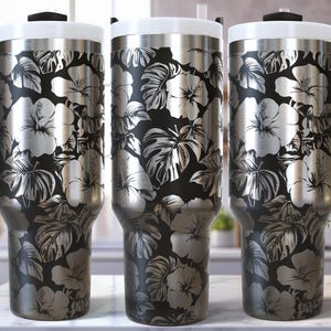 May include: Three stainless steel travel mugs with black handles and lids. The mugs feature a floral design of white hibiscus flowers and leaves on a black background. The mugs are displayed on a white surface.