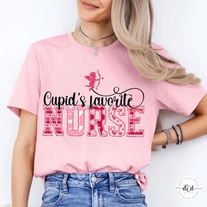 May include: A pink t-shirt featuring the phrase "Cupid's favourite NURSE". The word "NURSE" is in a block letter style with heart and pink patterns. A small cupid graphic is above the text.