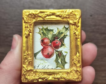May include: A miniature painting of holly berries and leaves in a gold frame. The artwork features three red berries and green leaves with gold accents. The frame has an ornate, textured design.