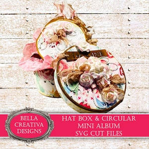 May include: A set of two decorative boxes with a floral design. The top box is a circular mini album with the word "Imagine" on it. The bottom box is a hat box with a pink and white floral design. The boxes are decorated with flowers, lace, and pearls. The boxes are on a white wooden background.