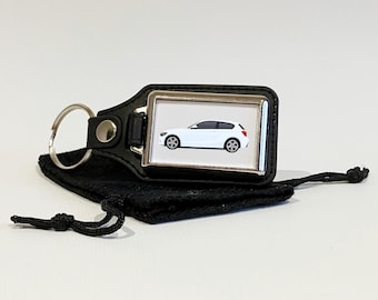 May include: A black leather keyring with a silver metal frame featuring a white car. The keyring comes with a black drawstring bag.