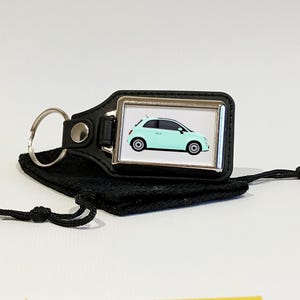 May include: A black leather keyring with a silver metal charm featuring a light blue car. The keyring comes with a black drawstring bag.