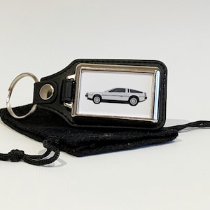 May include: A black leather keyring with a silver metal frame featuring a white DeLorean time machine. The keyring comes with a black drawstring bag.