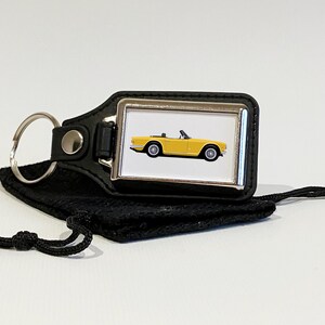 May include: A yellow convertible car keychain with a black leather strap and a silver metal keyring. The keychain is in a black pouch with a drawstring.
