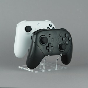 May include: A black and white video game controller stand with two controllers, one black and one white.