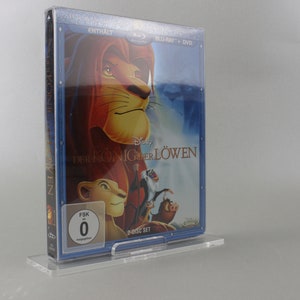 May include: A clear plastic case holds a DVD set of the Disney movie "The Lion King" in a blue and silver case. The front of the case features a picture of Simba, the lion cub, and the title "The Lion King" in German. The case also has a FSK rating of 0.
