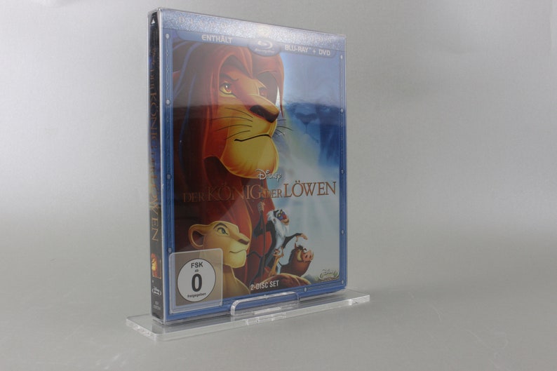 May include: A clear plastic case holds a DVD set of the Disney movie "The Lion King" in a blue and silver case. The front of the case features a picture of Simba, the lion cub, and the title "The Lion King" in German. The case also has a FSK rating of 0.