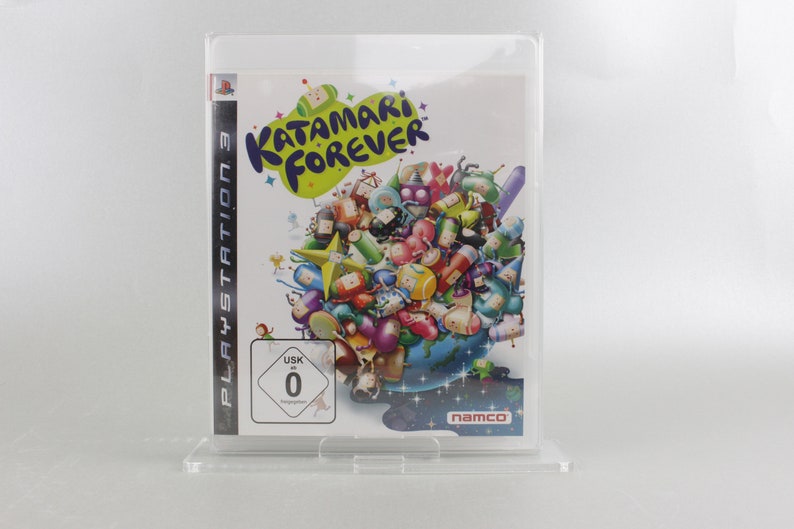 May include: A PlayStation 3 video game case with a colorful image of the game Katamari Forever. The game features a large, round, green ball with a smiling face and the words "Katamari Forever" written in white letters. The case is in a clear plastic protector.