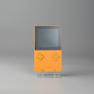 Op de afbeelding: Een feloranje handheld-videogamesysteem met een zwart scherm, een vierweg-directionele pad en vier knoppen.