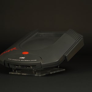 Peut inclure: Un système multimédia interactif 32 bits noir avec un bouton rouge et le texte "3DO" sur le devant.