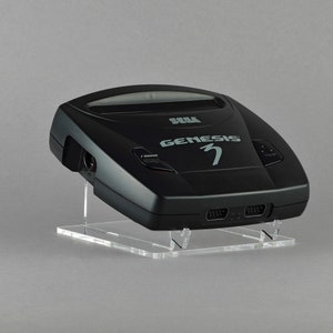 May include: A black Sega Genesis 3 video game console with a clear acrylic stand. The console has a black and silver design with the text "SEGA GENESIS 3" printed on the front.