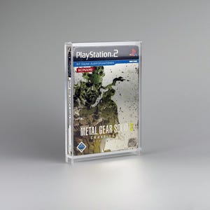 Könnte beinhalten: Eine transparente Kunststoffhülle mit einem PlayStation 2-Spiel. Das Spielcover zeigt eine grün-braune Illustration einer Figur aus Metal Gear Solid 3: Snake Eater. Der Titel und das Logo des Spiels sind sichtbar.