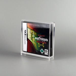 May include: A clear acrylic display case holding a Nintendo DS game cartridge. The game case features the "Metroid Prime Hunters" title with a green and red graphic. The case is designed to protect and showcase the game.