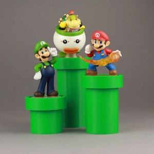 May include: Three green pipes with a green, blue, and white Mario character on the left pipe, a red Mario character on the right pipe, and a green, yellow, and brown Bowser character on the middle pipe.
