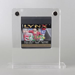 Könnte beinhalten: Ein transparentes Acryl-Display mit einer schwarzen und goldenen Lynx-Videospielkassette im Inneren. Die Spielkassette ist für das Spiel "Chip's Challenge".