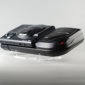 May include: A black Sega Genesis console with a black Sega CD add-on. The console is on a clear acrylic stand.