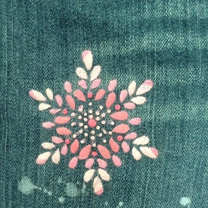 Puede incluir: Un diseño de copo de nieve bordado en una tela vaquera azul oscuro. El copo de nieve está hecho de hilo blanco y rosa.