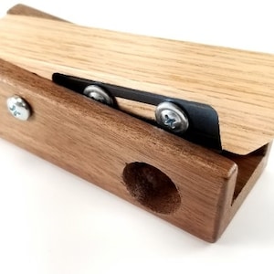 May include: A wooden tool with a dark brown base and a light brown top. The top has a metal blade with two screws. The base has a round hole.