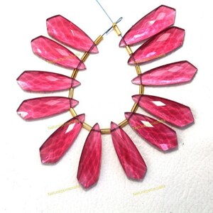 Puede incluir: Un conjunto de 12 colgantes de piedra preciosa de cuarzo rosa con forma de lágrima facetada. Los colgantes están enhebrados en anillos de salto de color dorado.