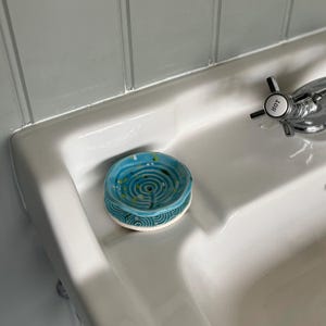 Op de afbeelding: Een blauwe en groene keramische zeepbak met een swirl-patroon. De bak staat in een witte porseleinen gootsteen.