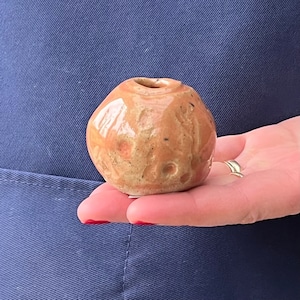May include: A small, round, ceramic vase with a speckled brown and orange glaze. The vase has a small opening at the top.