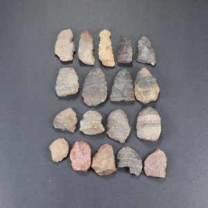May include: A collection of 18 arrowheads made of various types of stone, including flint, obsidian, and chert. The arrowheads are in various shades of brown, gray, and black. Some of the arrowheads have a pointed tip, while others have a rounded tip.