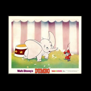 May include: A vintage lobby card featuring the animated character Dumbo, a light gray elephant with large ears, standing near a circus tent backdrop. Beside Dumbo is a small gray mouse wearing a red circus outfit. Text reads Walt Disney's DUMBO.