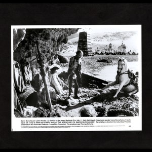 May include: A black and white photo of a scene from the movie "The Adventures of Baron Munchausen".  The Baron, played by John Neville, is standing on a beach with a horse and two other characters.  The scene is set in front of a large, imposing tower.