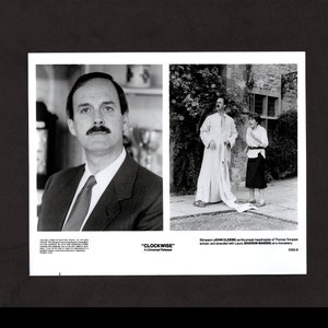 May include: Black and white photo of two actors from the movie "Clockwise". John Cleese is dressed in a white robe and Sharon Maiden is wearing a black skirt and white shirt. The text "Clockwise" and "A Universal Release" is at the bottom of the photo.