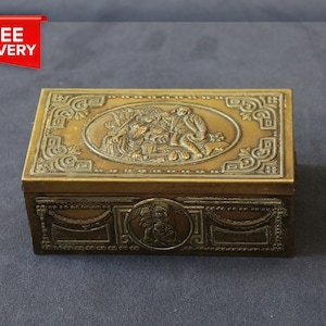 Scatola per sigarette ornata in ottone. Scatola per gingilli in legno e ottone. Scatola in ottone goffrato. Scatola per gioielli in ottone con base in legno. Scatola in ottone con cherubini.