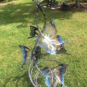 May include: A metal sculpture of four butterflies in a spiral design. The butterflies are made of stainless steel and have a blue and purple iridescent finish.