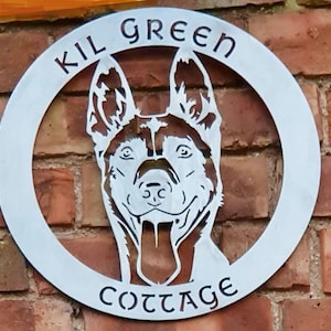 May include: A silver metal sign with a dog's head cut out in the center. The sign reads "Kil Green Cottage" in a decorative font.