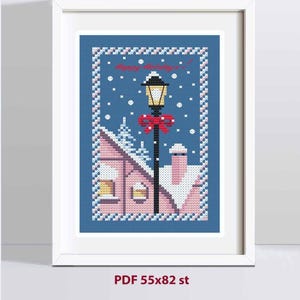 May include: A framed cross-stitch pattern featuring a winter scene with a black lamppost adorned with a red bow, a pink house with snow-covered roofs, and falling snowflakes against a blue background. The text reads Happy Holidays! PDF 55x82 st.