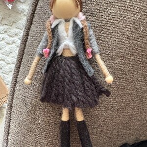 May include: A felt doll with brown hair, a grey jacket, a white shirt, a black skirt, and black boots.