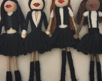Könnte beinhalten: Vier handgefertigte Puppen mit Holzköpfen, roten Lippen und schwarzen Garnhaaren. Jede Puppe trägt ein schwarzes Outfit mit Rock und einem weißen oder cremefarbenen Oberteil. Die Puppen haben Arme und Beine aus Garn und schwarze Perlenfüße.