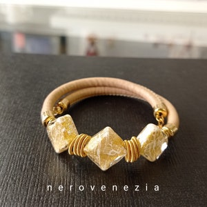 May include: A beige leather bracelet with three gold-toned square beads. The beads have a white, crackled glass design.