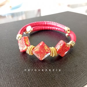 May include: Red leather bracelet with three gold-rimmed, red glass beads with gold flecks. The beads are square-shaped with rounded corners. The bracelet is wrapped twice around the wrist.