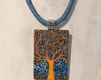 Puede incluir: Un collar azul y dorado con un colgante rectangular que presenta un árbol estilizado con ramas en espiral. El colgante está hecho de vidrio y tiene un diseño de mosaico.