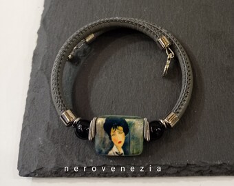 Op de afbeelding: Een grijze leren wikkelarmband met een rechthoekig middelpunt met een vintage portret van een vrouw. De armband heeft zwarte kralen en zilverkleurige metalen accenten. De tekst "nerovenezia" staat onderaan.