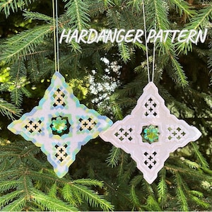 May include: Two diamond-shaped ornaments featuring Hardanger pattern embroidery. The left ornament displays blue, green, and yellow thread work with a central green crystal. The right ornament features white thread work with a central green crystal.