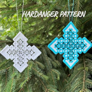 Peut inclure: Deux ornements en forme de croix Hardanger, un blanc et un turquoise, sont suspendus à un arbre. Les ornements présentent des motifs ajourés complexes et sont suspendus par des fils blancs. Le texte "HARDANGER PATTERN" est au-dessus des ornements.