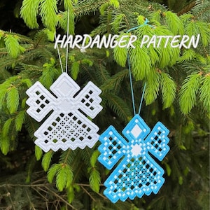 Peut inclure: Deux ornements en forme d'ange, motif Hardanger, un blanc et un bleu, suspendus à un arbre. Les anges présentent un motif géométrique avec des détails ajourés. Le texte "HARDANGER PATTERN" est au-dessus des ornements.