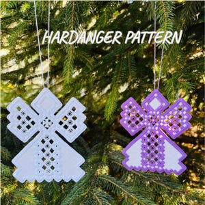 Peut inclure: Deux ornements en forme d'ange, motifs Hardanger, suspendus à un arbre. L'un est blanc, l'autre violet et blanc. Les ornements ont un design géométrique avec des détails ajourés, suspendus par des fils blancs. Le texte "HARDANGER PATTERN" est au-dessus.