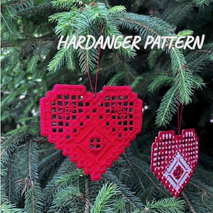 Peut inclure: Deux ornements Hardanger rouges en forme de cœur suspendus à un sapin de Noël. Le plus grand ornement présente un motif ajouré détaillé. Le plus petit a un motif blanc et rouge. Le texte "HARDANGER PATTERN" est au-dessus des ornements.